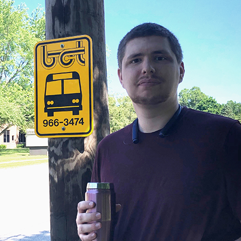 Young man at buss stop holding a to-go mug.