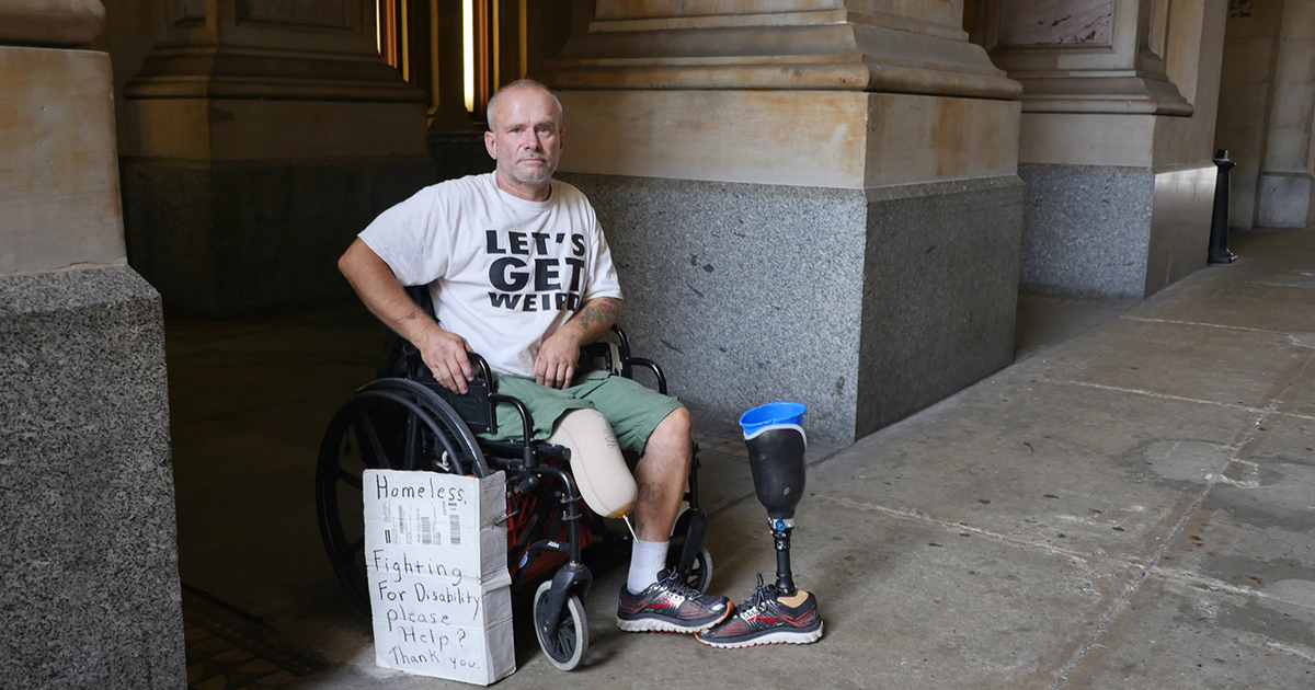 man in a wheelchair on sidewalk with his prosthetic leg next to him, and a sign that reads: Homeless. Fighting for disability. Please Help. Thank you." 