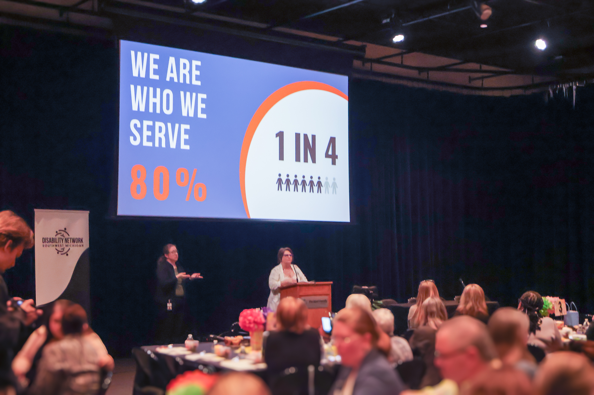 A projector screen showing a statistic of 1 in 4 people have a disability. It reads we are who we serve, 80%.