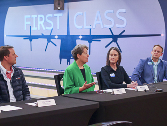 Four individuals wearing business attire, seated at a table for a press conference.