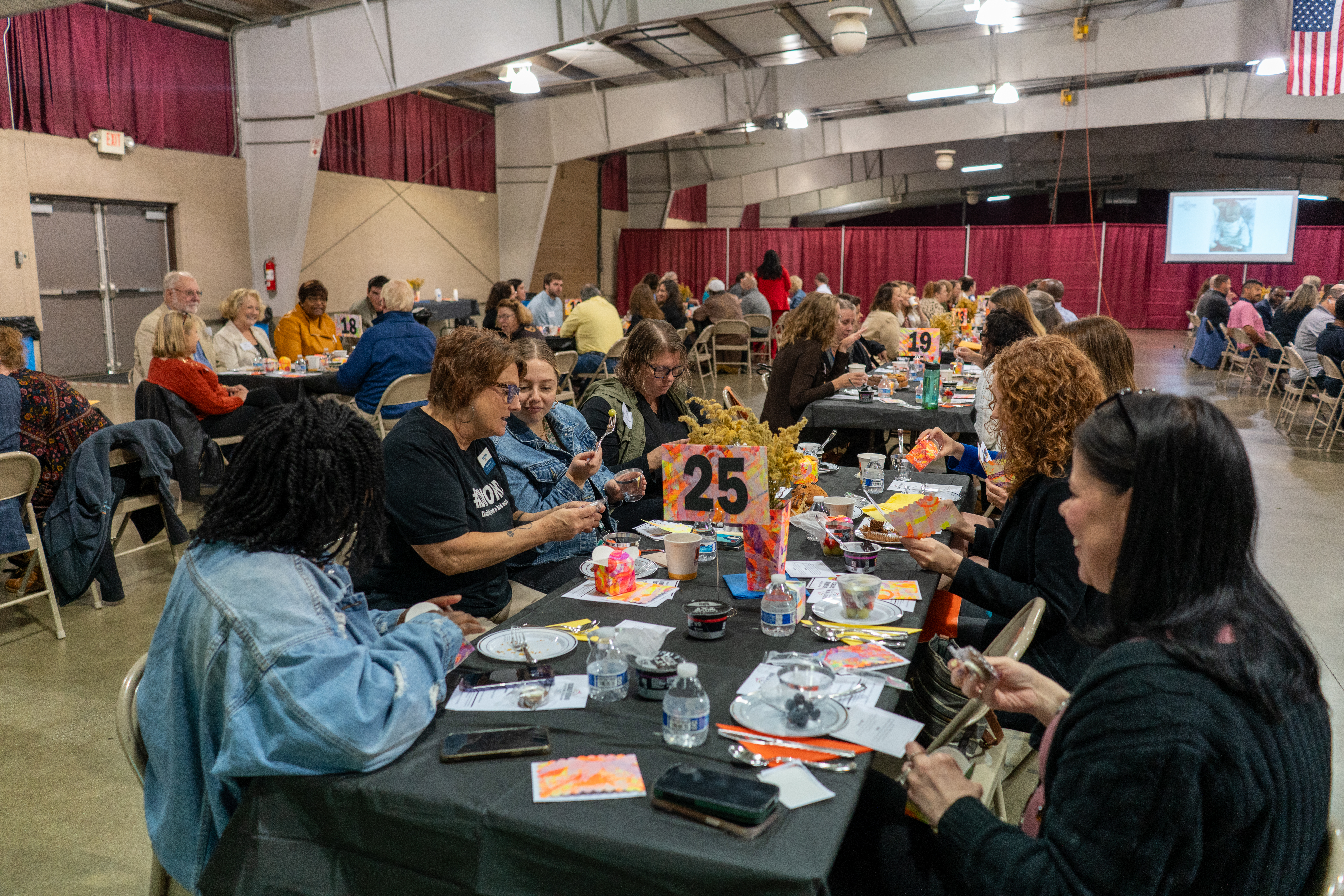 A diverse group of people gathered in a large room, seated at breakfast tables.