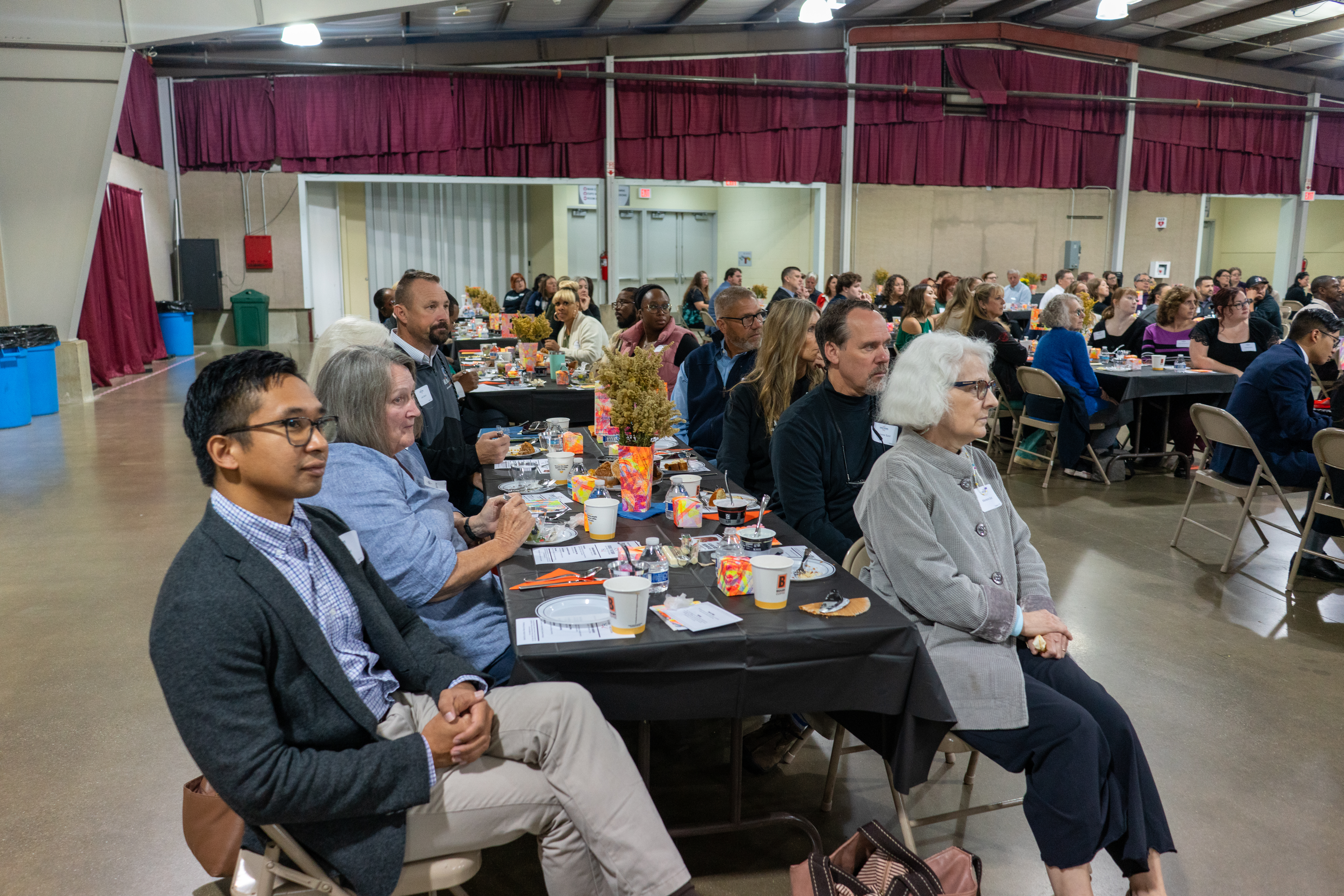 A diverse group of people gathered in a large room, seated at breakfast tables.