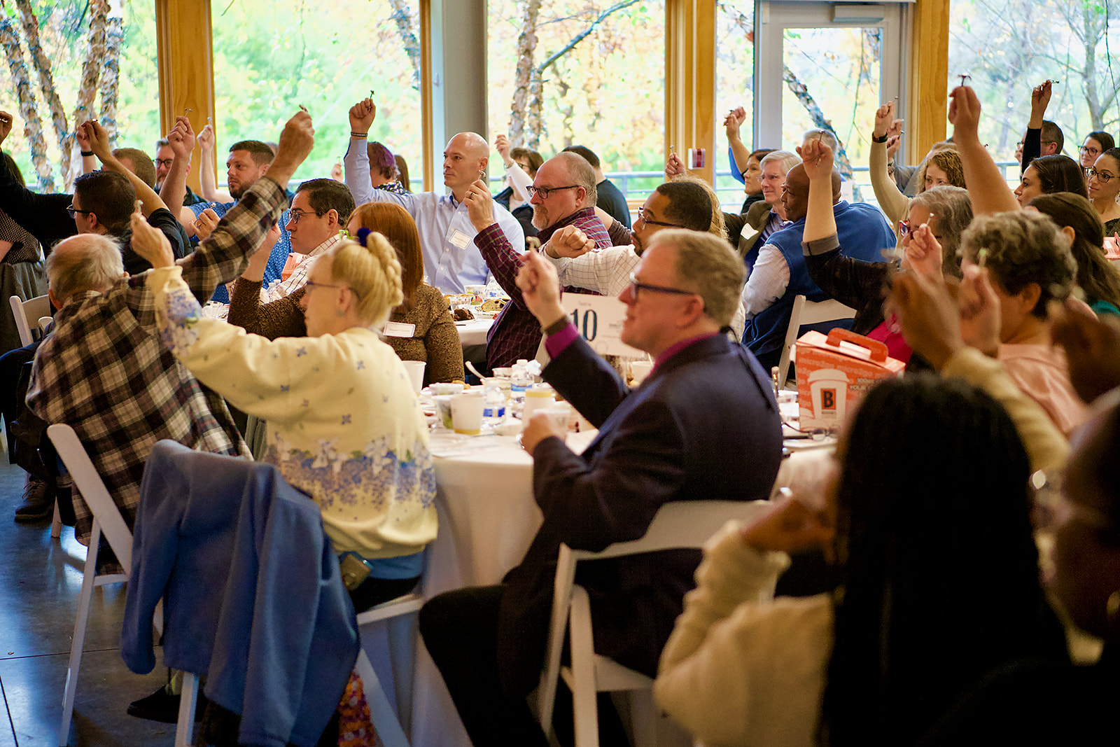 Diverse community members seated in a large room, holding a small metal keychain in the air with their hands.