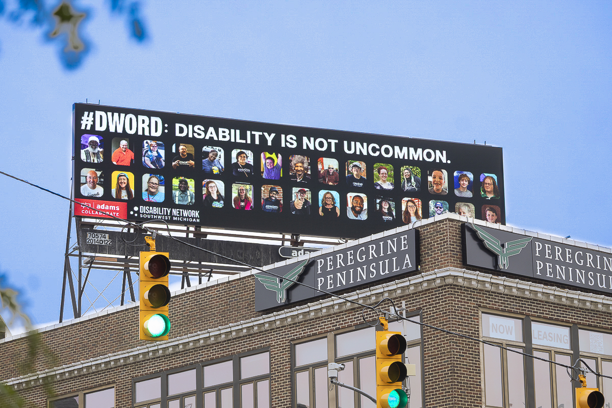 An electronic sign featuring many images of people's faces. Text: #DWord: Disability is not uncommon.