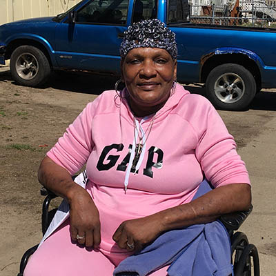 A woman with dark skin wearing a leopard print hat and a pink sweat suit seated in a wheelchair.