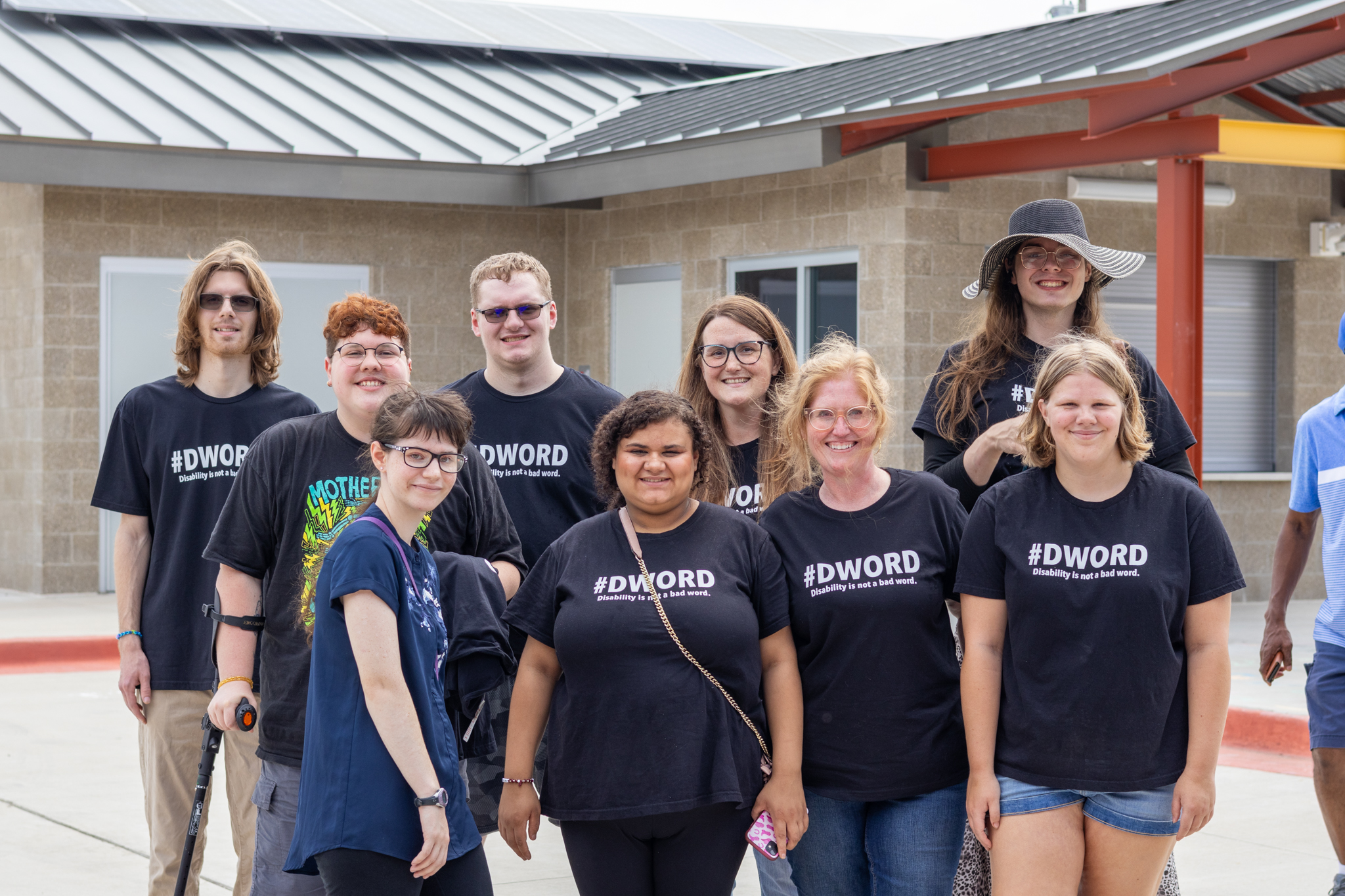 A diverse group of young adults wearing black shirts reading #DWord Disability is not a bad word.