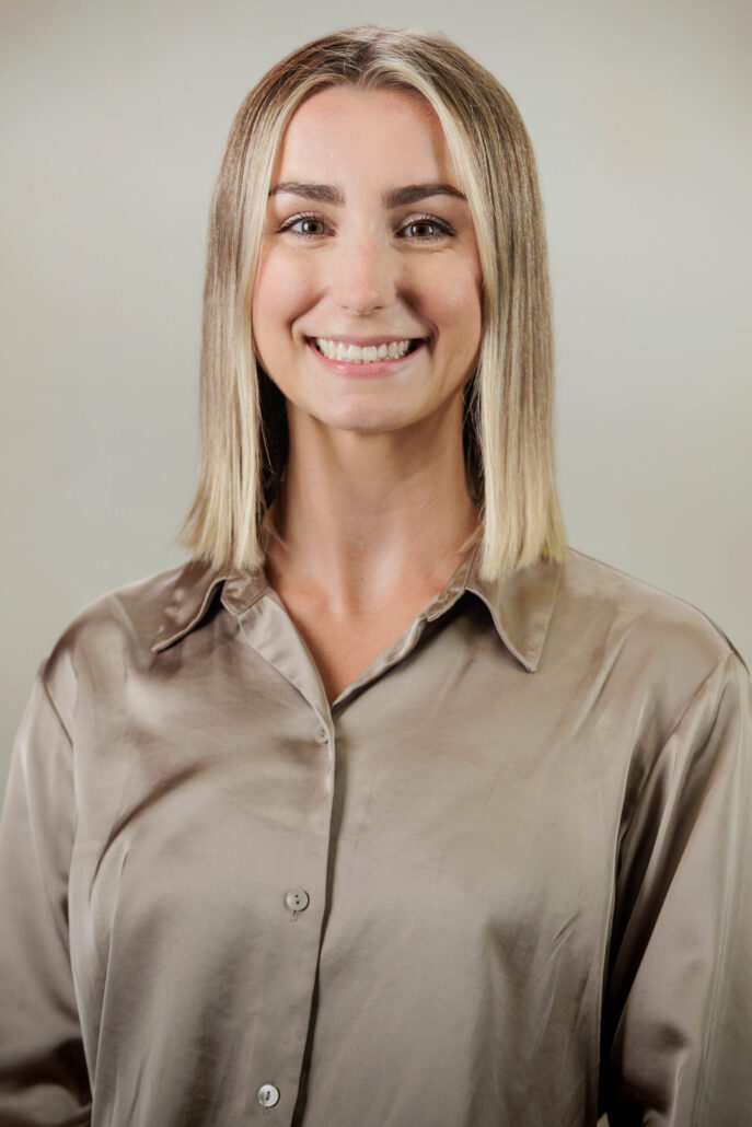 A blonde young woman with shoulder length hair, wearing a beige top.