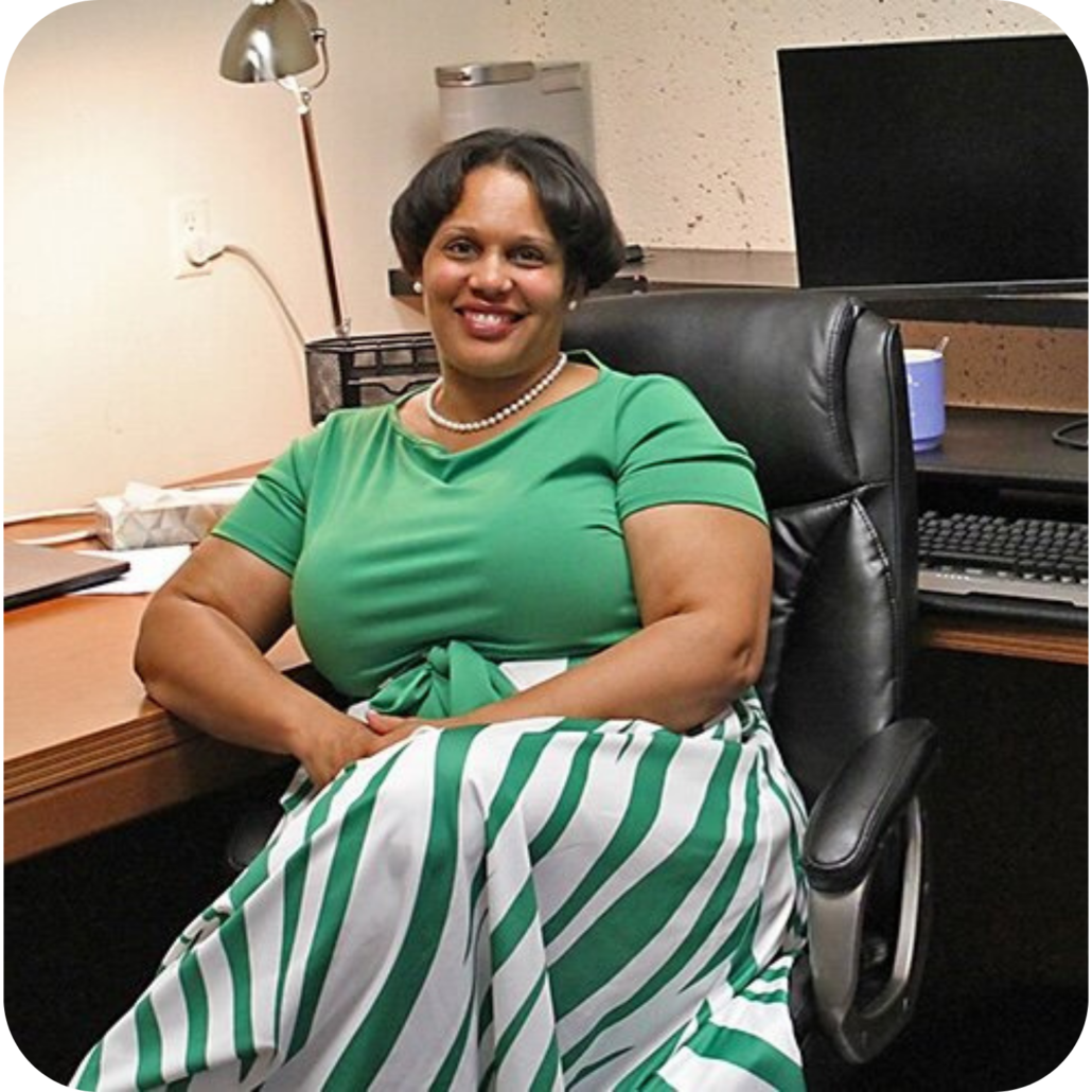 President & CEO, Kelley Kellis, a Black woman with short hair, wearing a green top and a green and white striped skirt.
